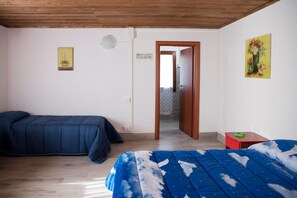 A bedroom with a wooden ceiling, two beds, a door leading to another room, and a small table with a green object on it. - B&B Sentiero Romantico (Eboli)