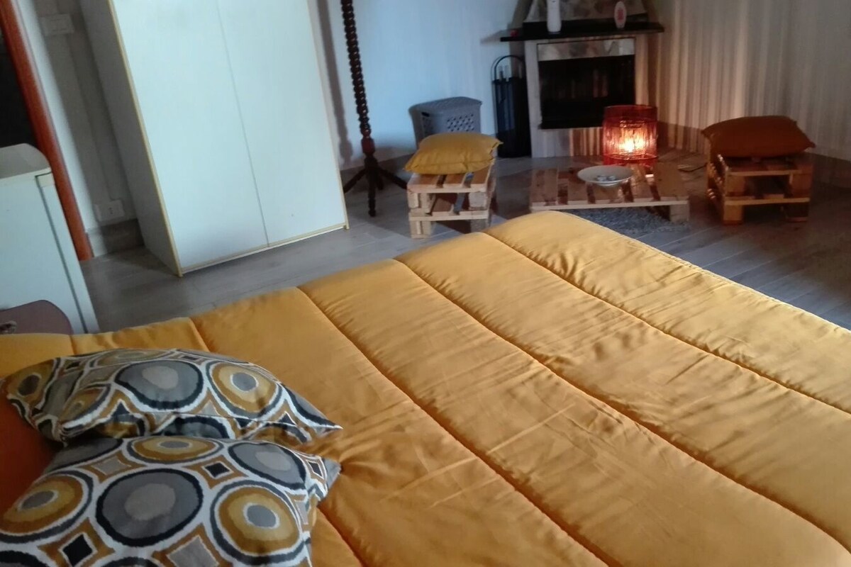 A bedroom with a large bed, a wooden chair, a small table, and a fireplace.