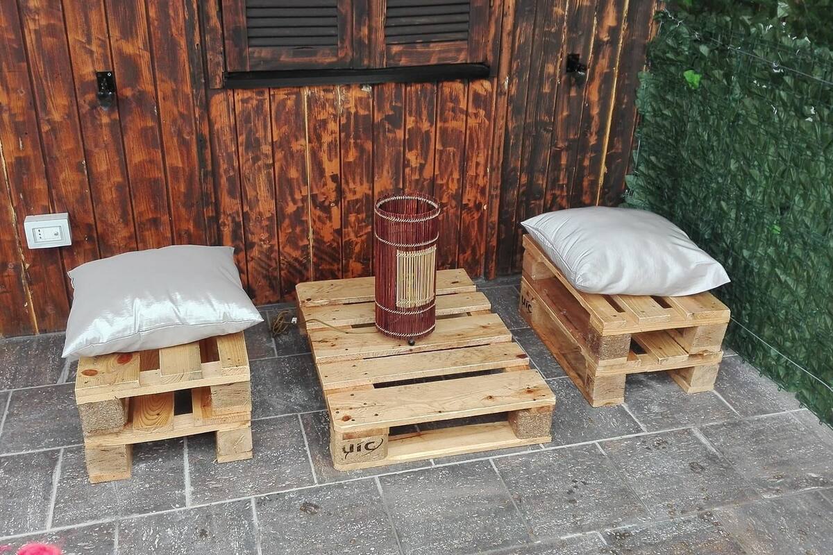 A rustic outdoor seating area with two wooden stools and a central table, each with a white cushion.