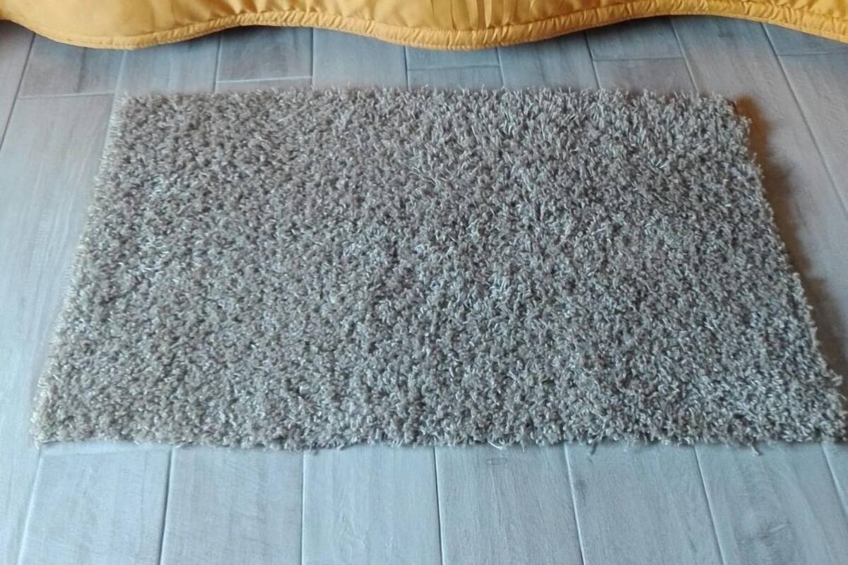 A bed with a yellow bedspread and patterned pillows, a grey shaggy rug, and a wooden floor.