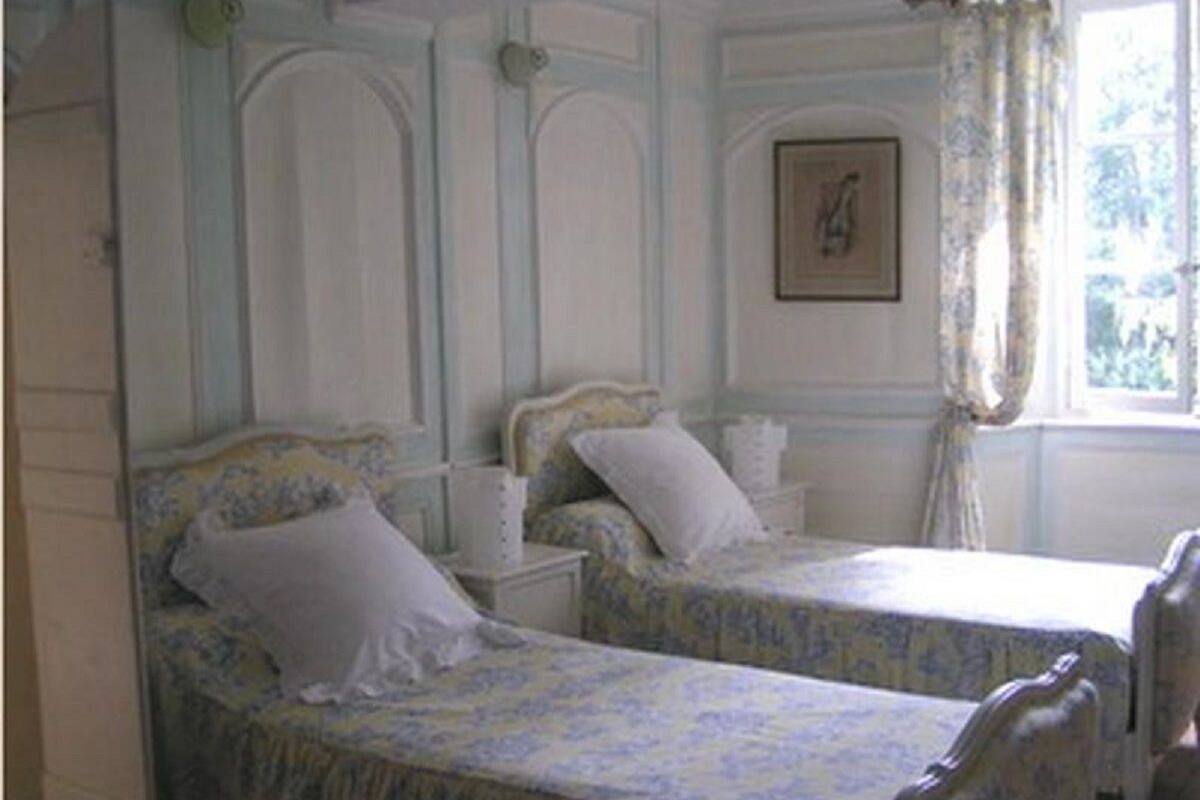 A bedroom with two single beds, a nightstand, a framed picture on the wall, and a window with curtains.