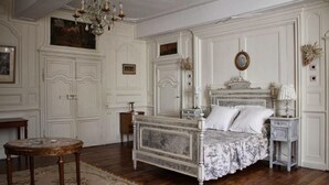 Een klassieke slaapkamer met een marmeren bed, gedetailleerd wandpaneel, een kroonluchter en een ronde tafel.
