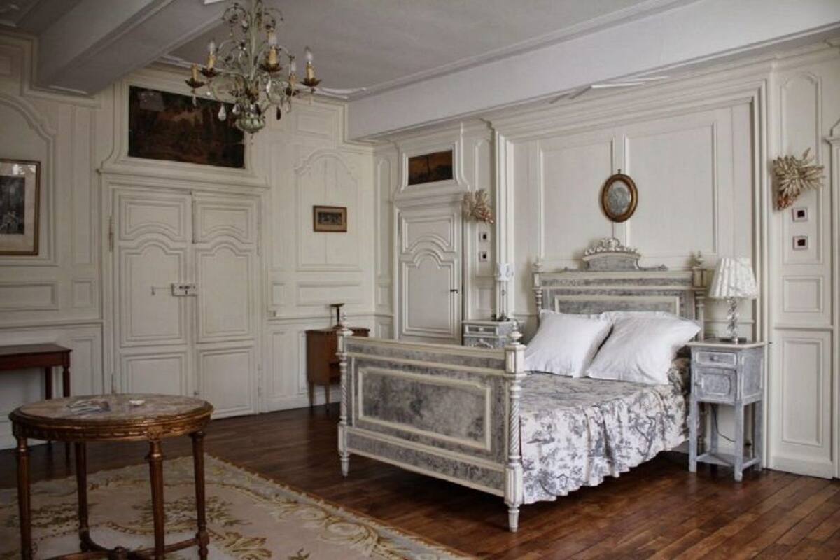 A classic bedroom with a marble bed, ornate wall paneling, a chandelier, and a round table.