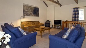 A cozy living room with blue sofas, a wooden coffee table, a fireplace, and a television. - Green Door - Marigold (Port Isaac)