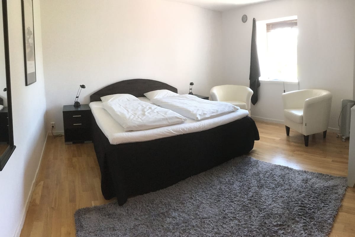 A bedroom with a bed, bedside tables, a chair, a radiator, and a window.