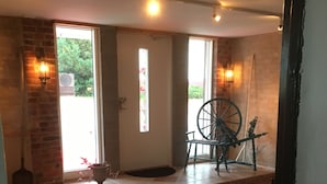 A room with a large window, a door with a stained glass design, a wooden chair, a decorative wheel, and a tiled floor. - Borrby frö - Bed & Breakfast (Borrby)