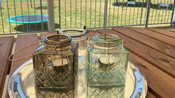 Two glass jars with metal lids on a tray, placed on a wooden table with a view of a fenced outdoor area. - Borrby frö - Bed & Breakfast (Borrby)