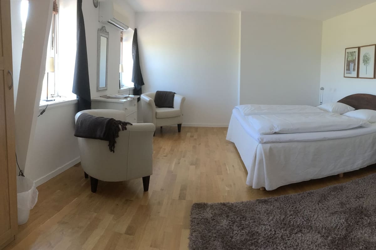 A bedroom with a bed, bedside table, chair, and a large window.