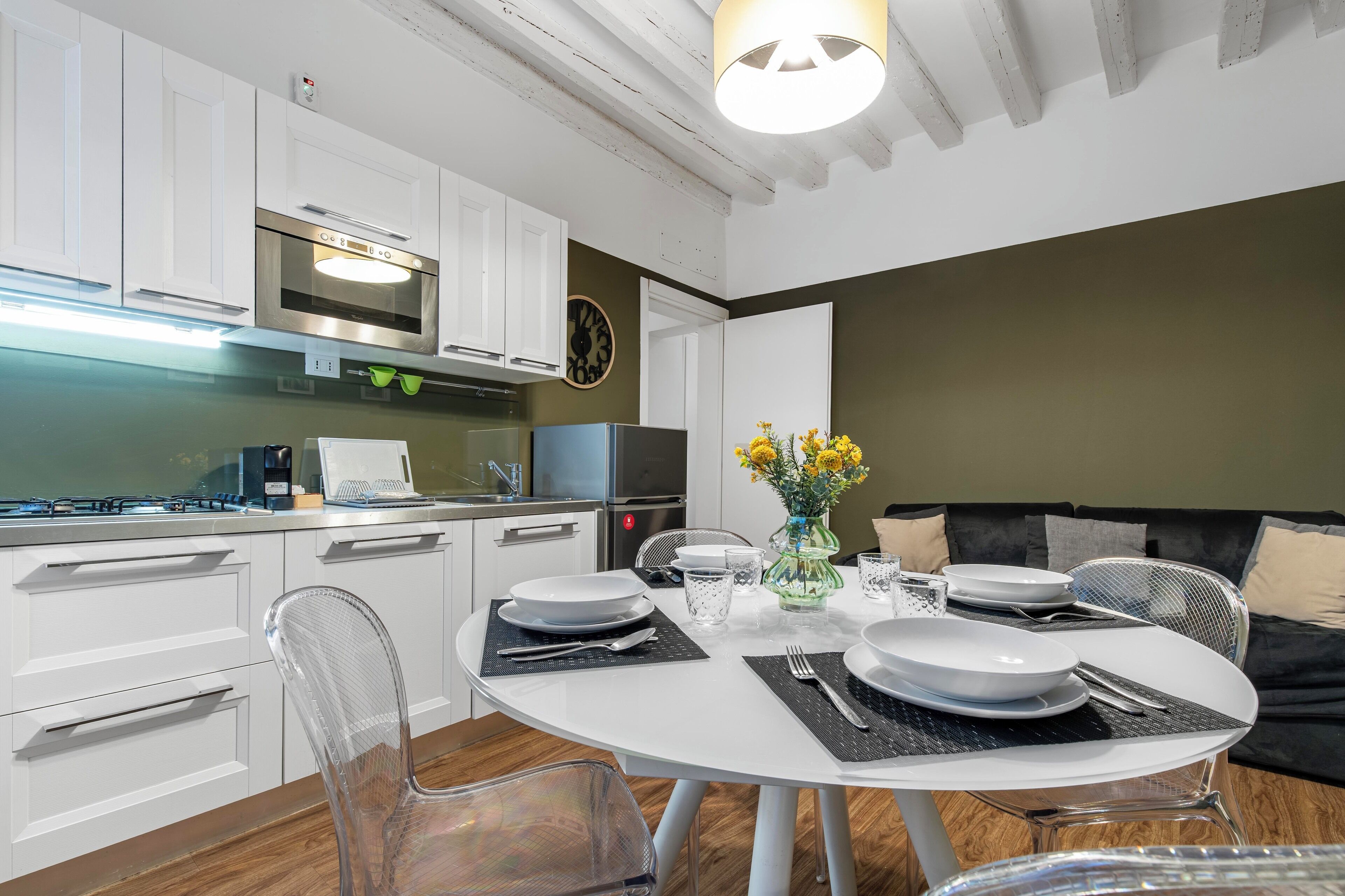 Una cocina moderna con armarios blancos, horno empotrado y un comedor con una mesa redonda para dos.