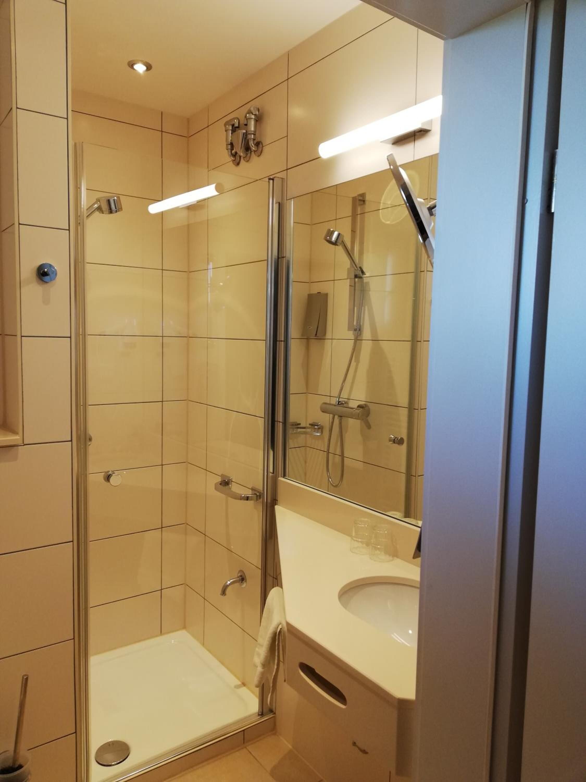A modern bathroom with a glass-enclosed shower, a white sink, and a mirror.