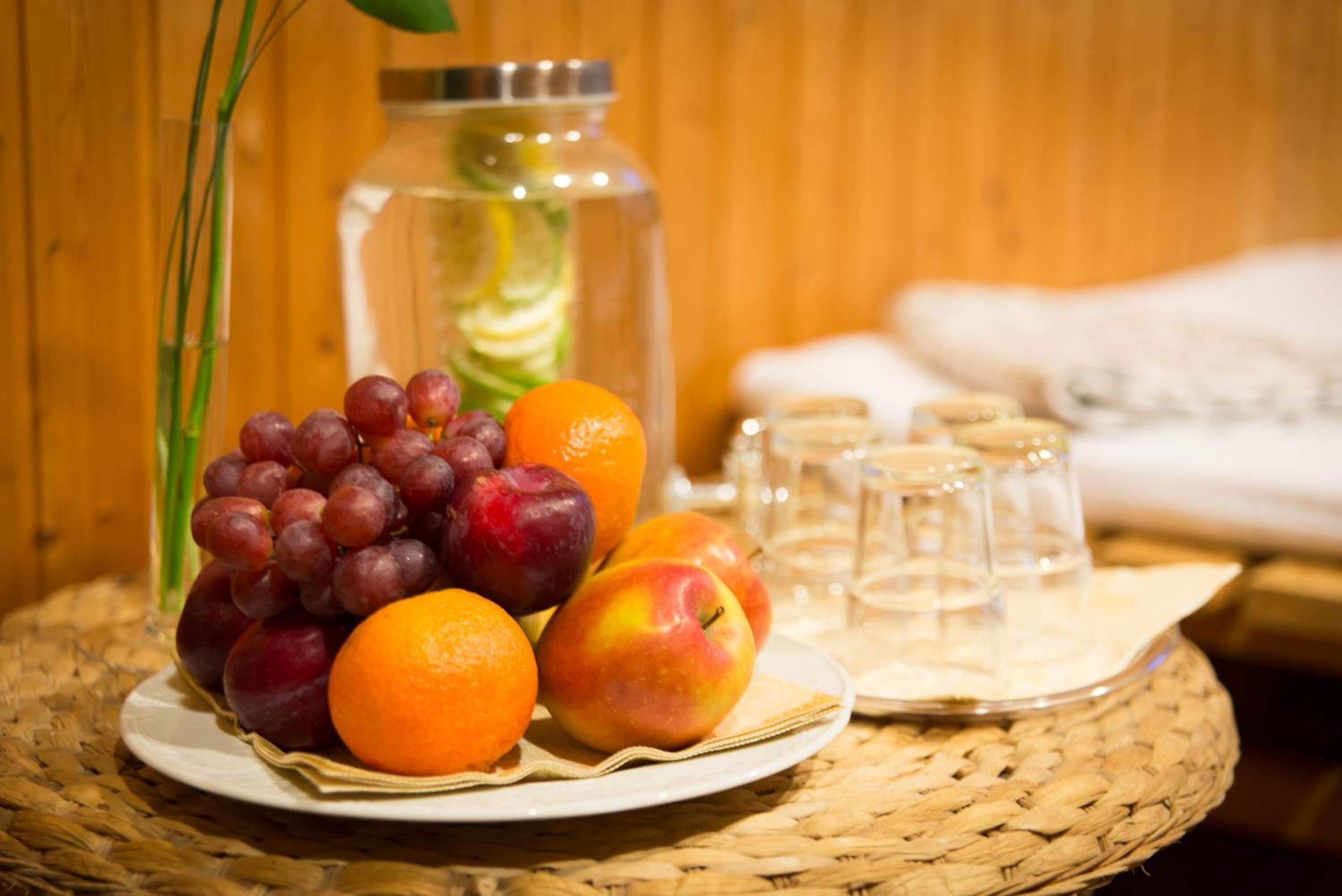 A plate of fruits, a glass jar, and several glasses on a woven mat.