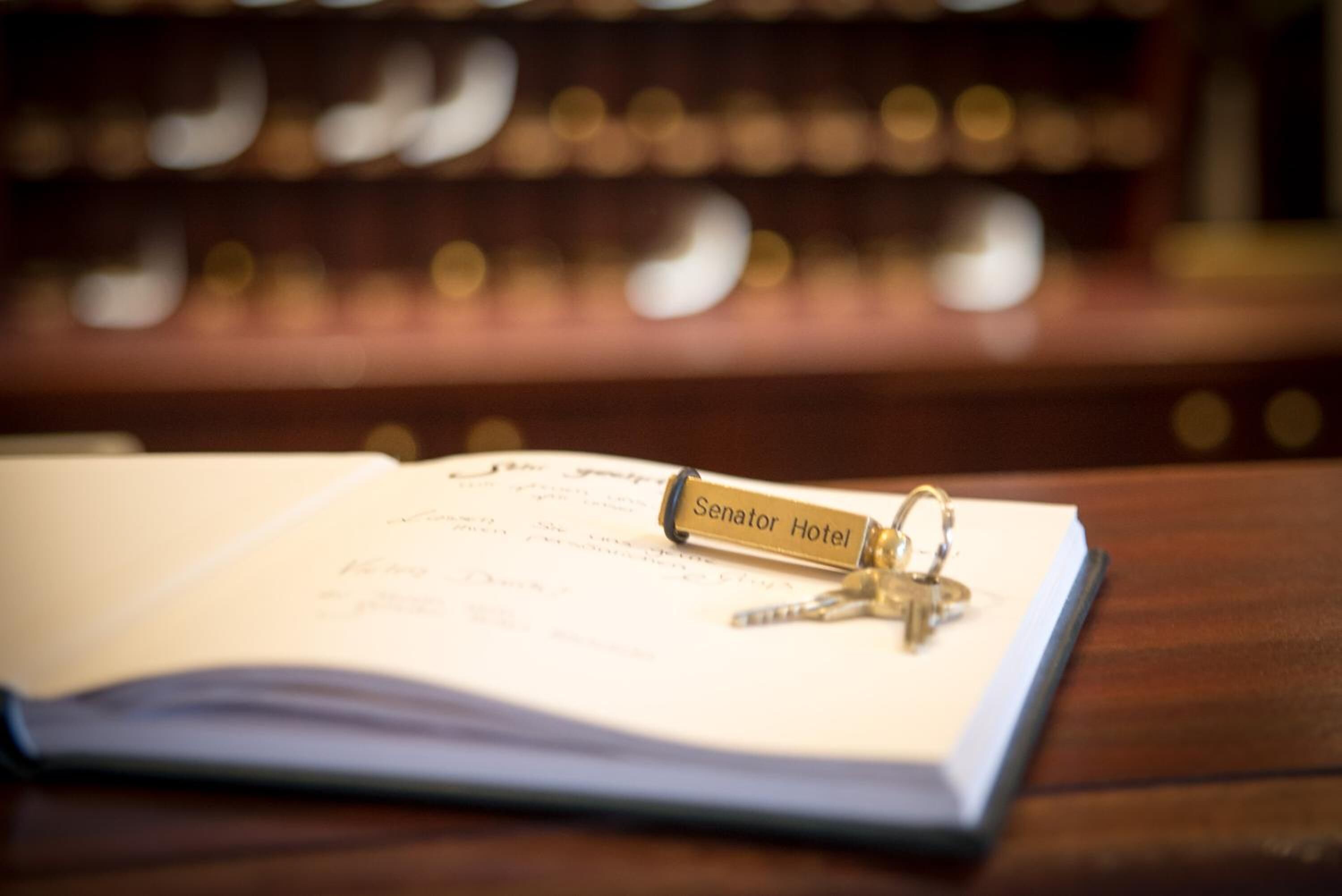 An open book with a keychain labeled "Senator Hotel" on a wooden surface.