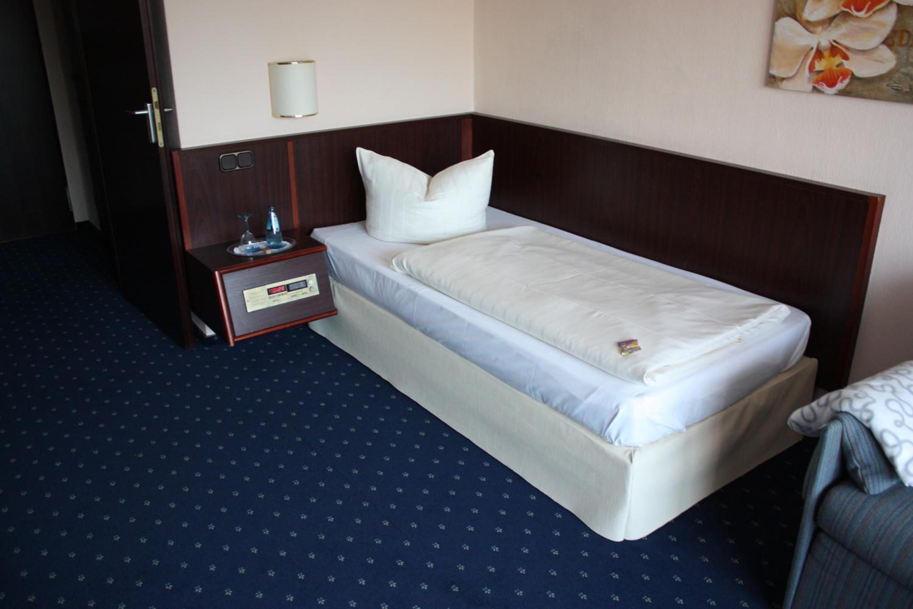 A single bed with a wooden headboard, a bedside table with a lamp, and a wall-mounted light fixture.