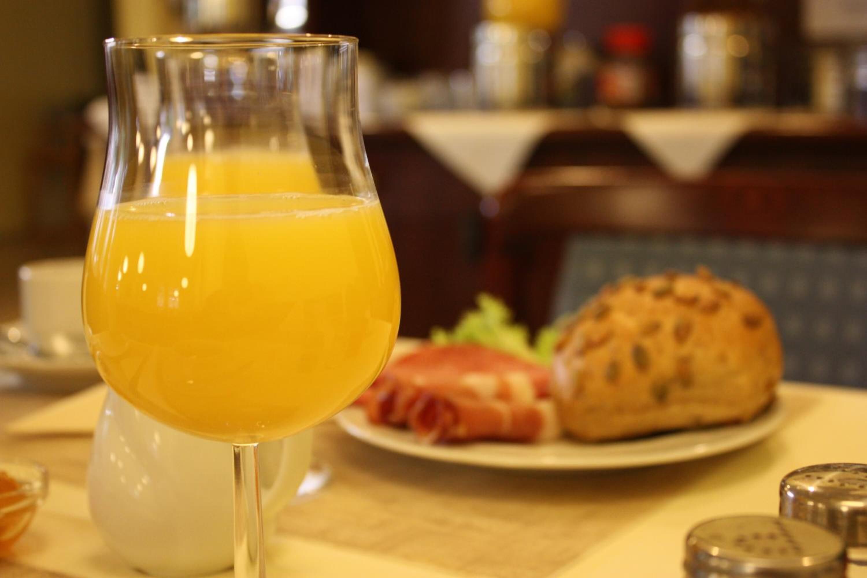 A glass of orange juice on a table with a plate of food and condiments.