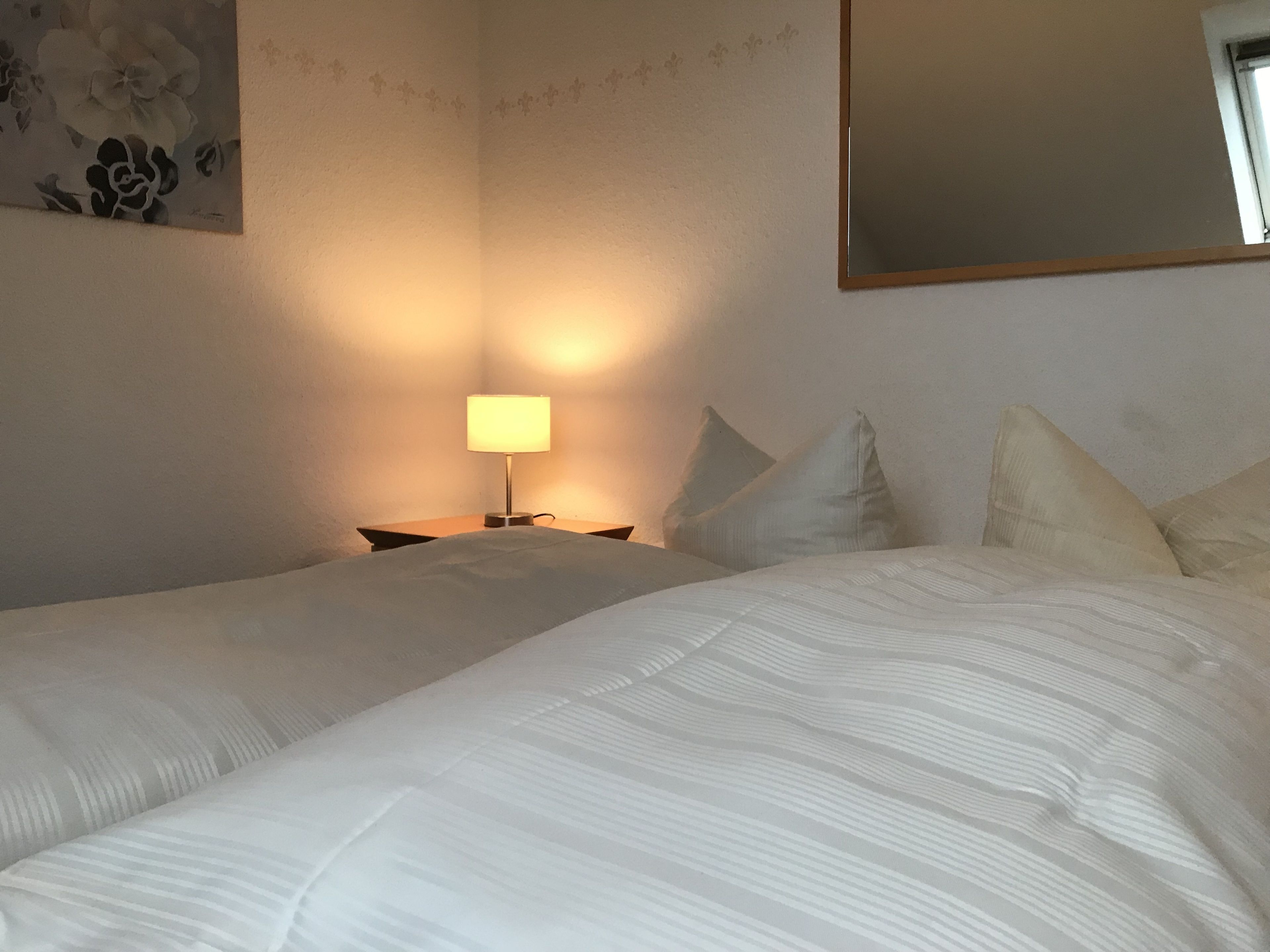 A hotel room with two beds, a bedside table with a lamp, and a large mirror on the wall.