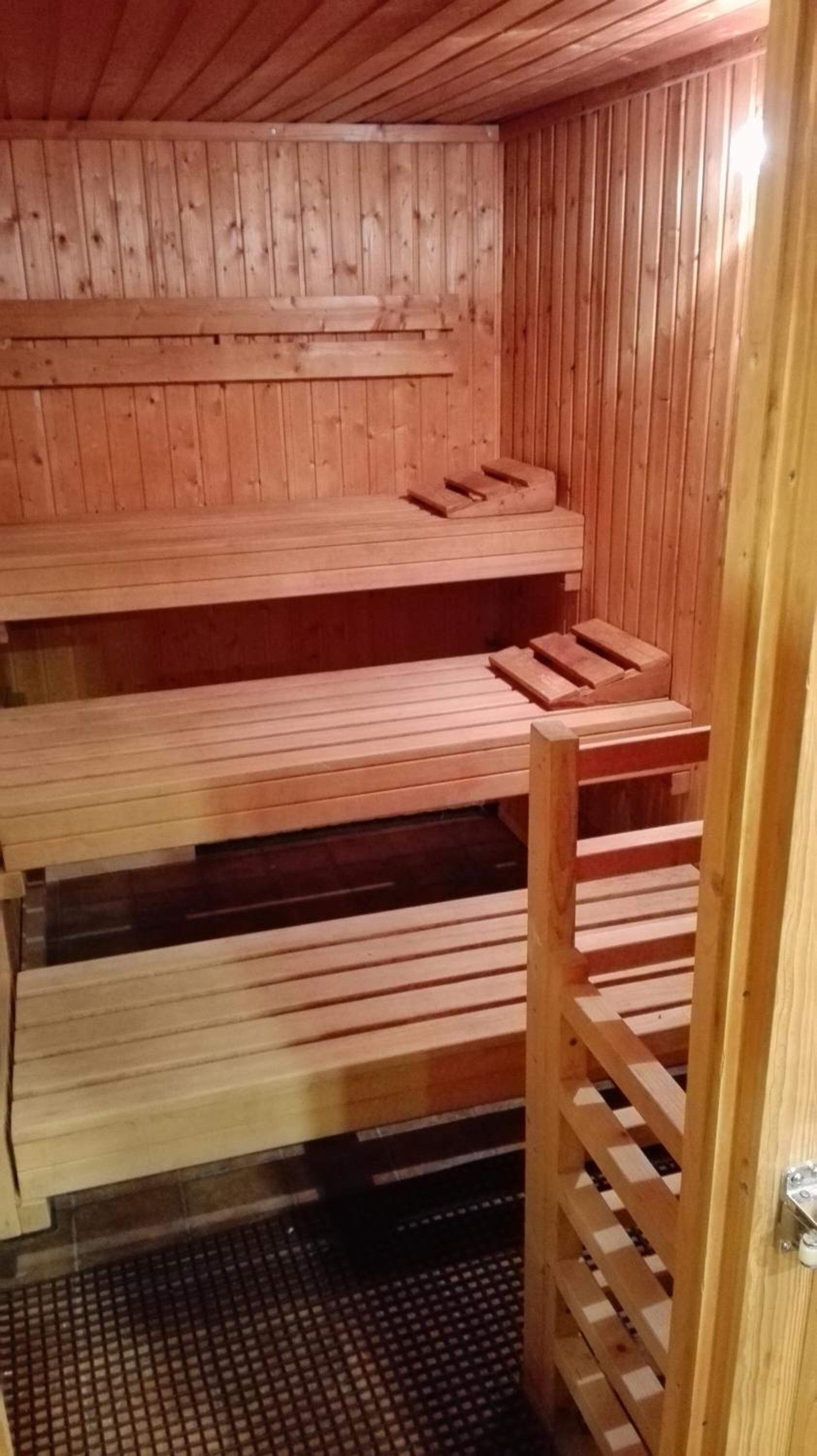 A sauna with wooden benches and a metal grid floor.
