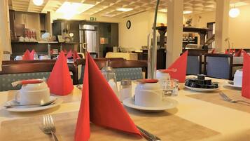A dining area with tables set for two, featuring red napkins, white plates, and silverware.