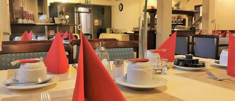 Comedor con mesas dispuestas para dos, con servilletas rojas, platos blancos y cubertería.