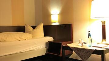 Quarto de hotel com uma cama, mesa de cabeceira, mesa com abajur e luminária na parede.