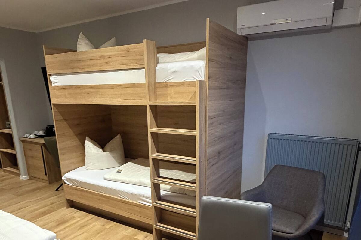 A bunk bed with a desk and chair, a radiator, and a small table with a laptop.