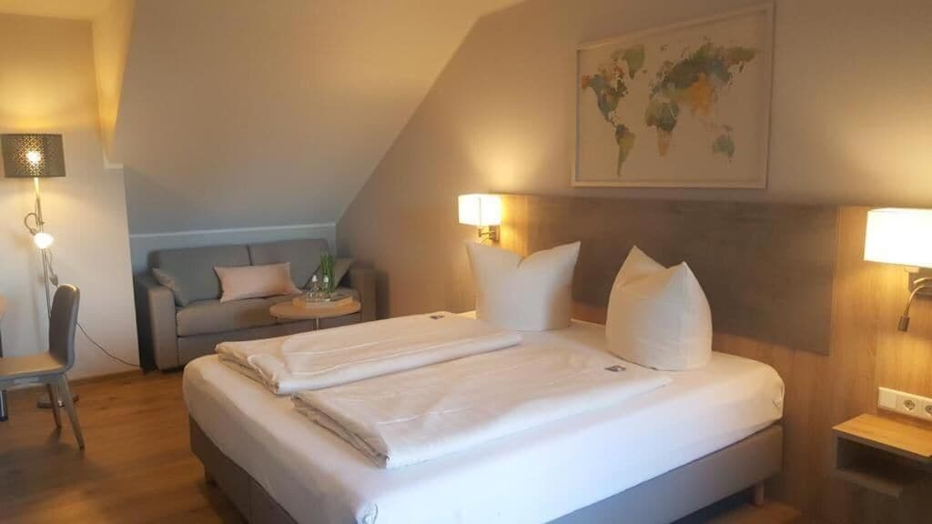 A hotel room with a large bed, a desk, and a chair. There are two bedside lamps and a world map on the wall.
