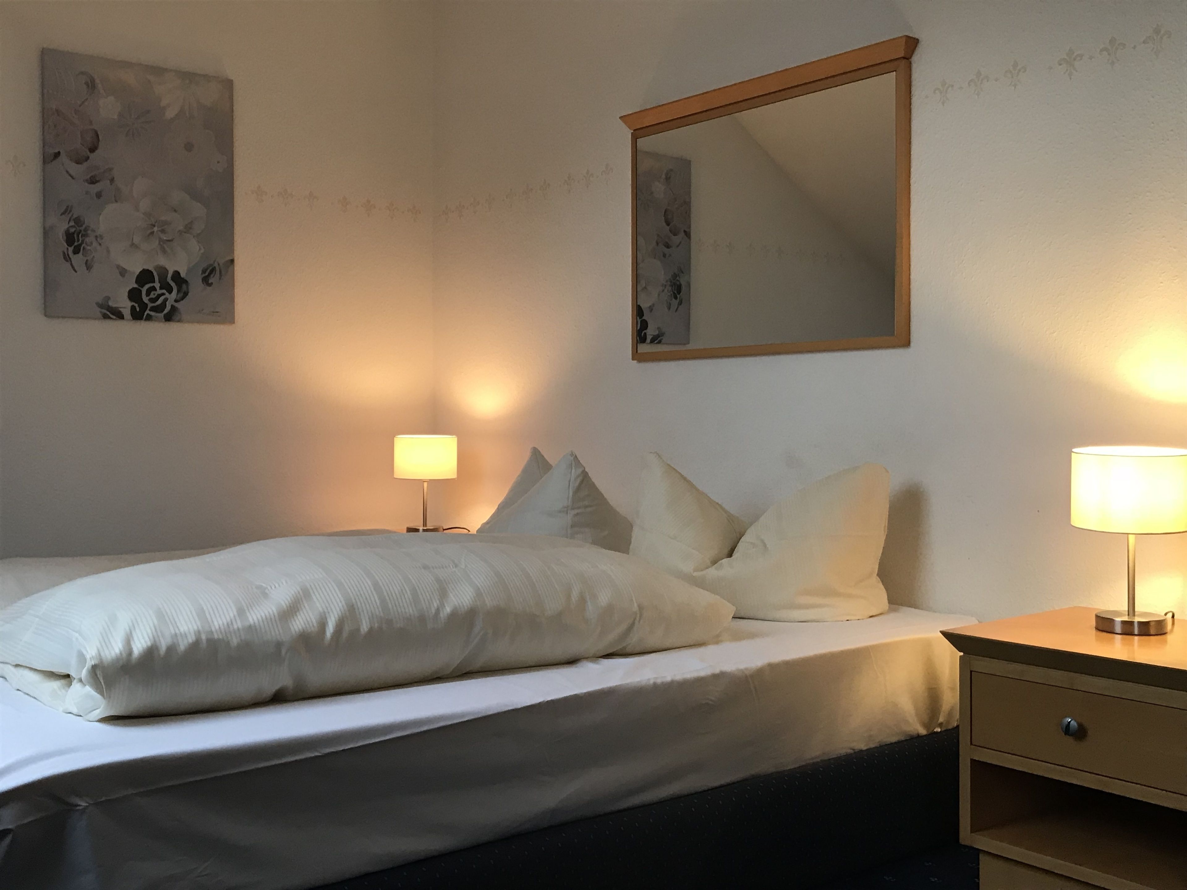 Un lit bien fait, avec des oreillers, une table de chevet avec une lampe et un miroir fixé au mur.