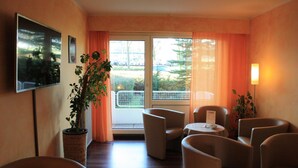 Une chambre d’hôtel avec un balcon, une télévision, une plante en pot et plusieurs chaises.