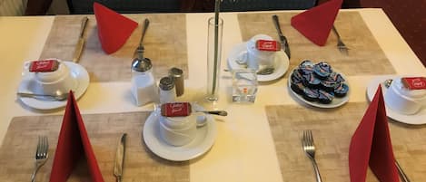 Mesa dispuesta para dos con mantel blanco, servilletas rojas y un centro de mesa con una flor blanca.