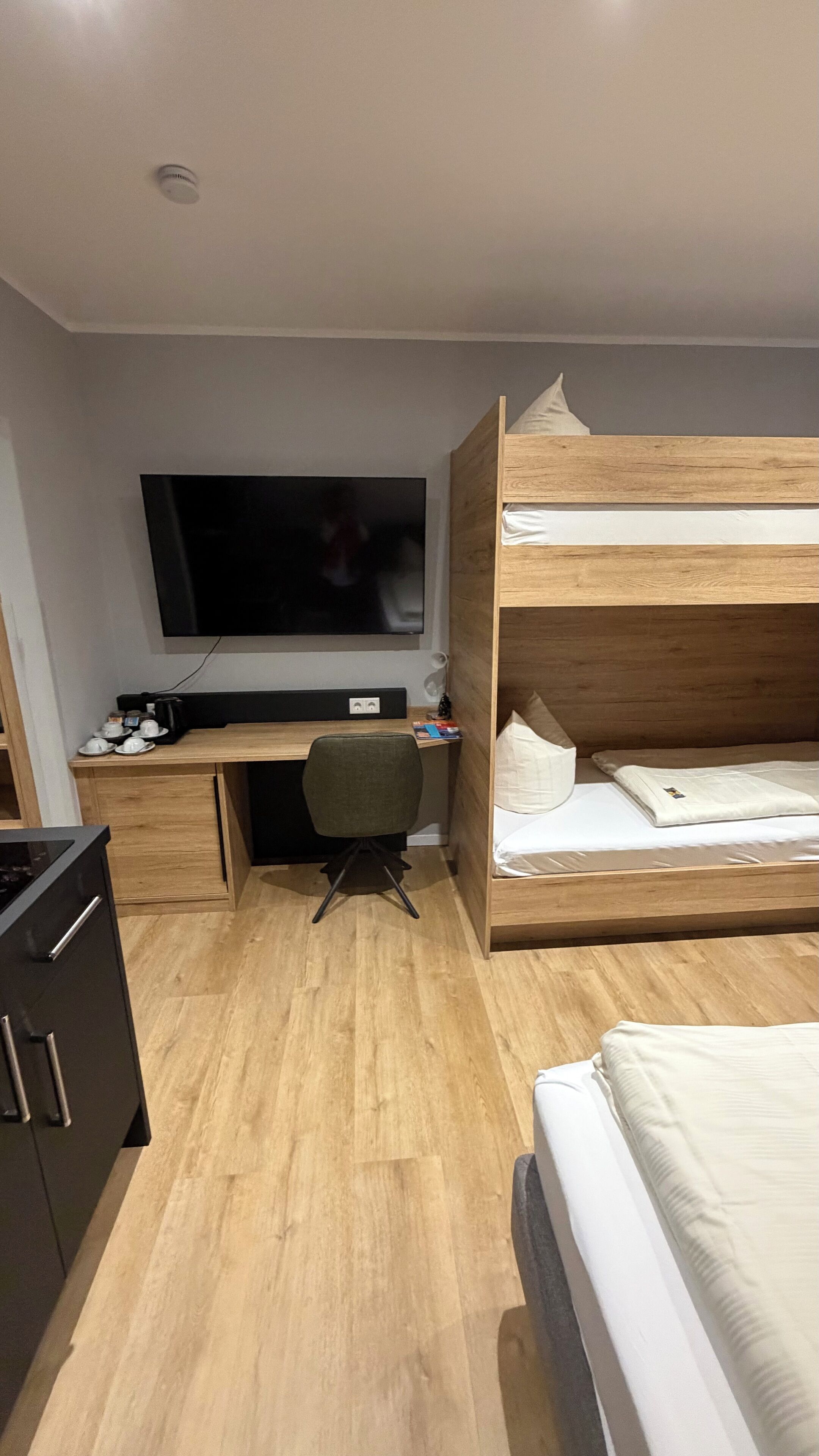 Ein kleines Hotelzimmer mit Etagenbett, Schreibtisch mit Stuhl, Fernseher und Küchenzeile.