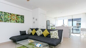 Un salón moderno con un sofá gris oscuro, cojines estampados en verde y amarillo, una mesa de centro de vidrio y una alfombra verde.