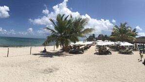 Una playa de arena blanca, palmeras y un velero a lo lejos.