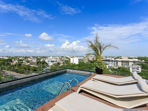 A rooftop pool with lounge chairs and a view of a cityscape.