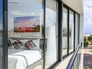 Un balcón con cama, ventanas amplias y vista al mar.