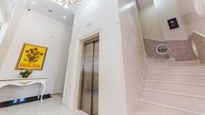 Un interior moderno con una escalera, un ascensor de pared y una lámpara decorativa en el techo.