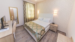 Habitación de hotel con cama, mesita de noche, lámpara, escritorio con computadora, silla y cortinas.