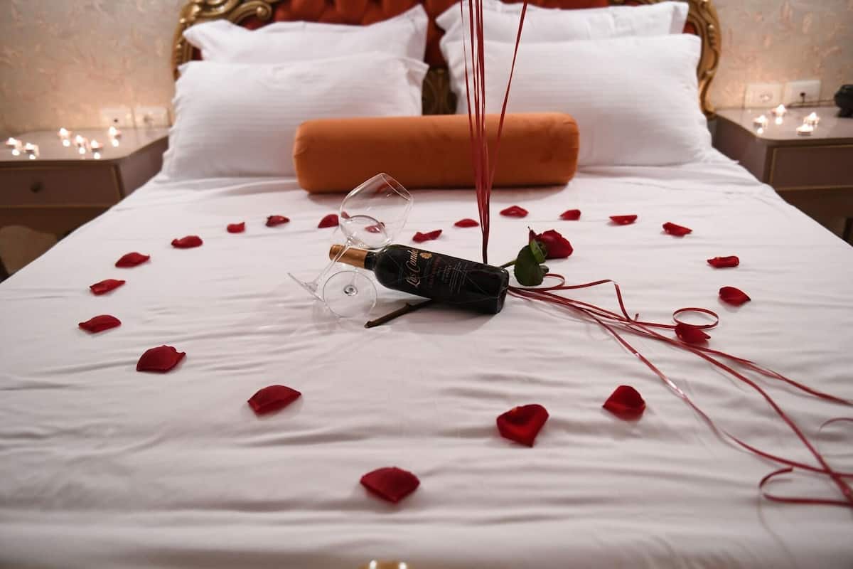 A bed with rose petals, a wine bottle, and a glass on it.