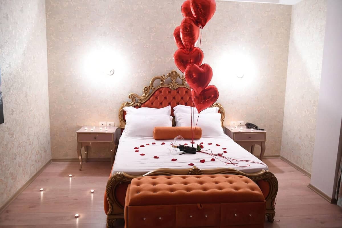 A hotel room with a large bed, a bedside table, a nightstand, and a decorative heart balloon arrangement.