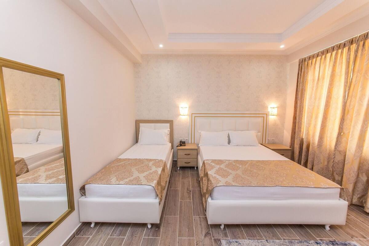 A hotel room with two single beds, a mirror, bedside lamps, a nightstand, and a patterned rug.