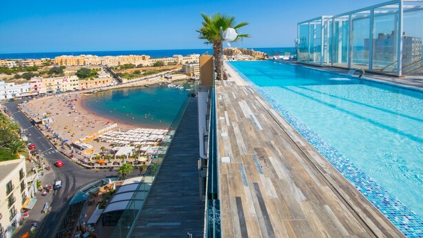 A high-rise hotel with a rooftop pool overlooking a beach and cityscape. - H Hotel (St. Julian's)