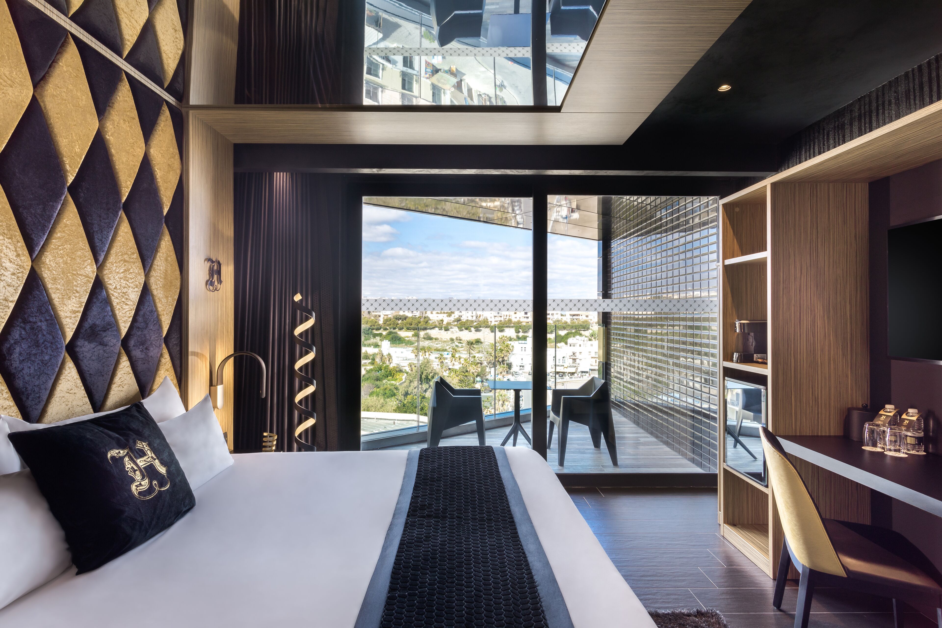Ein modernes Hotelzimmer mit einem großen Bett, Blick auf die Stadt und einem Balkon mit Sitzgelegenheiten.