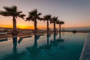 A pool with palm trees and lounge chairs, surrounded by a fence, with a sunset in the background.
