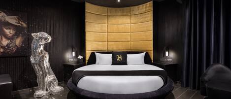 A modern bedroom with a curved bed, dark walls, and a gold accent wall.
