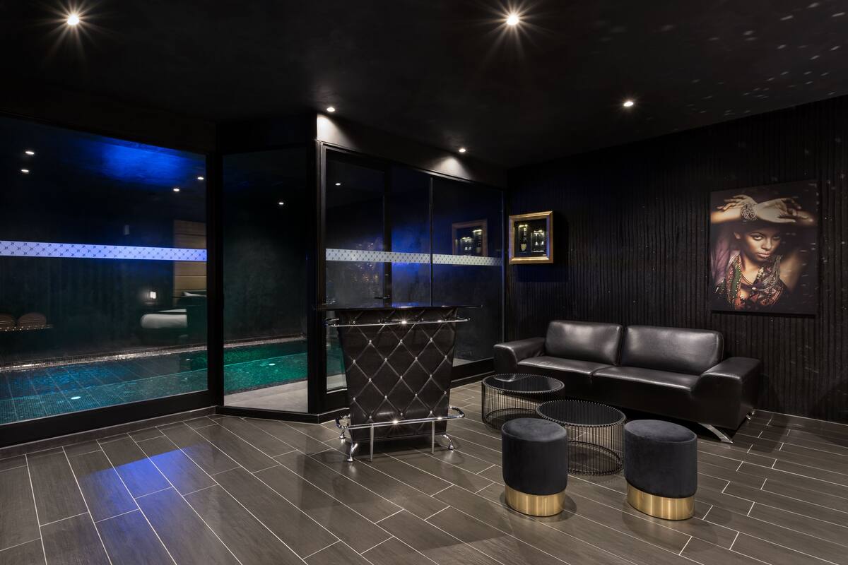 Un moderno espacio de spa con un jacuzzi envuelto en vidrio, un sofá de cuero negro y una pequeña mesa redonda.