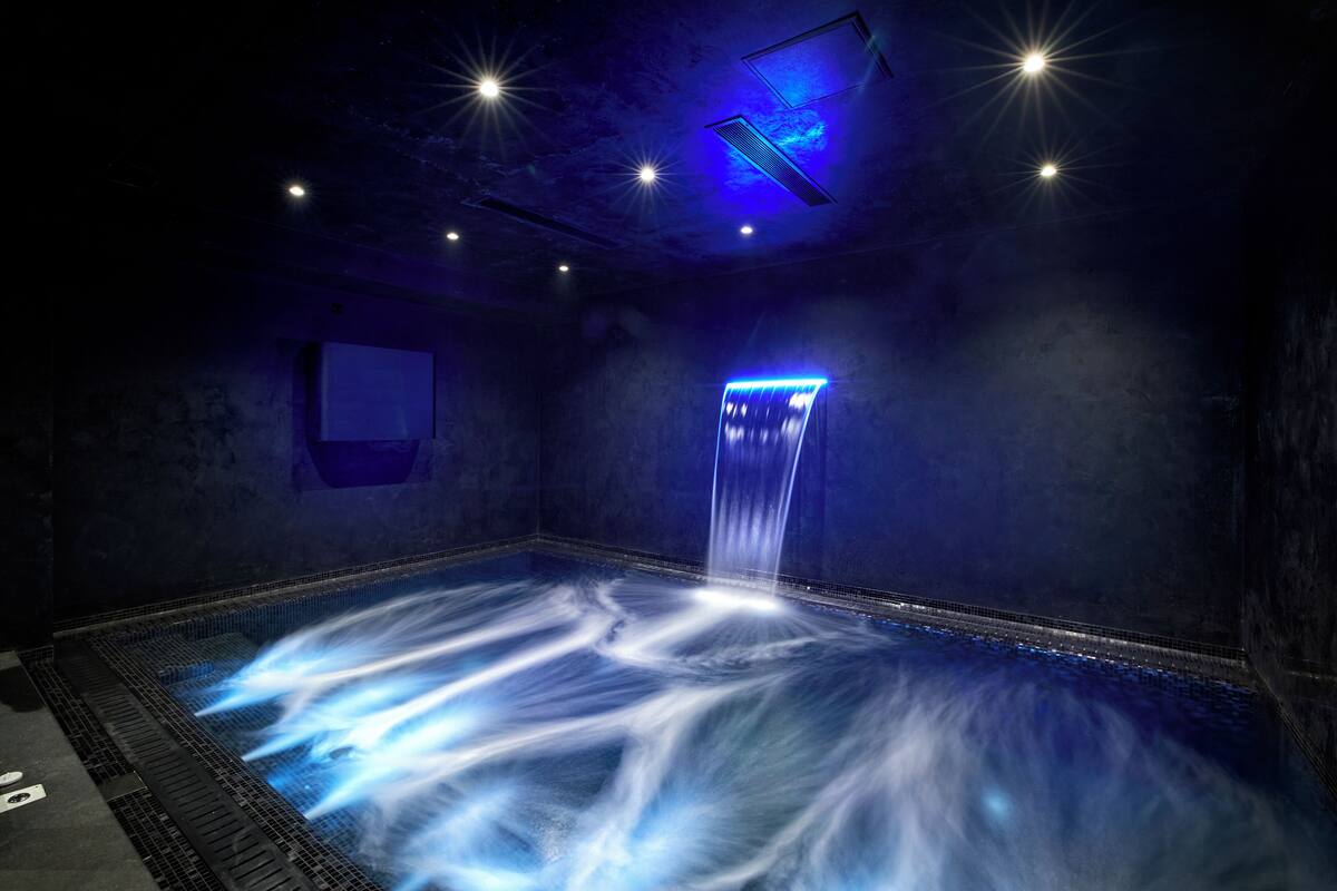 Una habitación tenuemente iluminada, con una fuente iluminada en azul y un pequeño ventanal.
