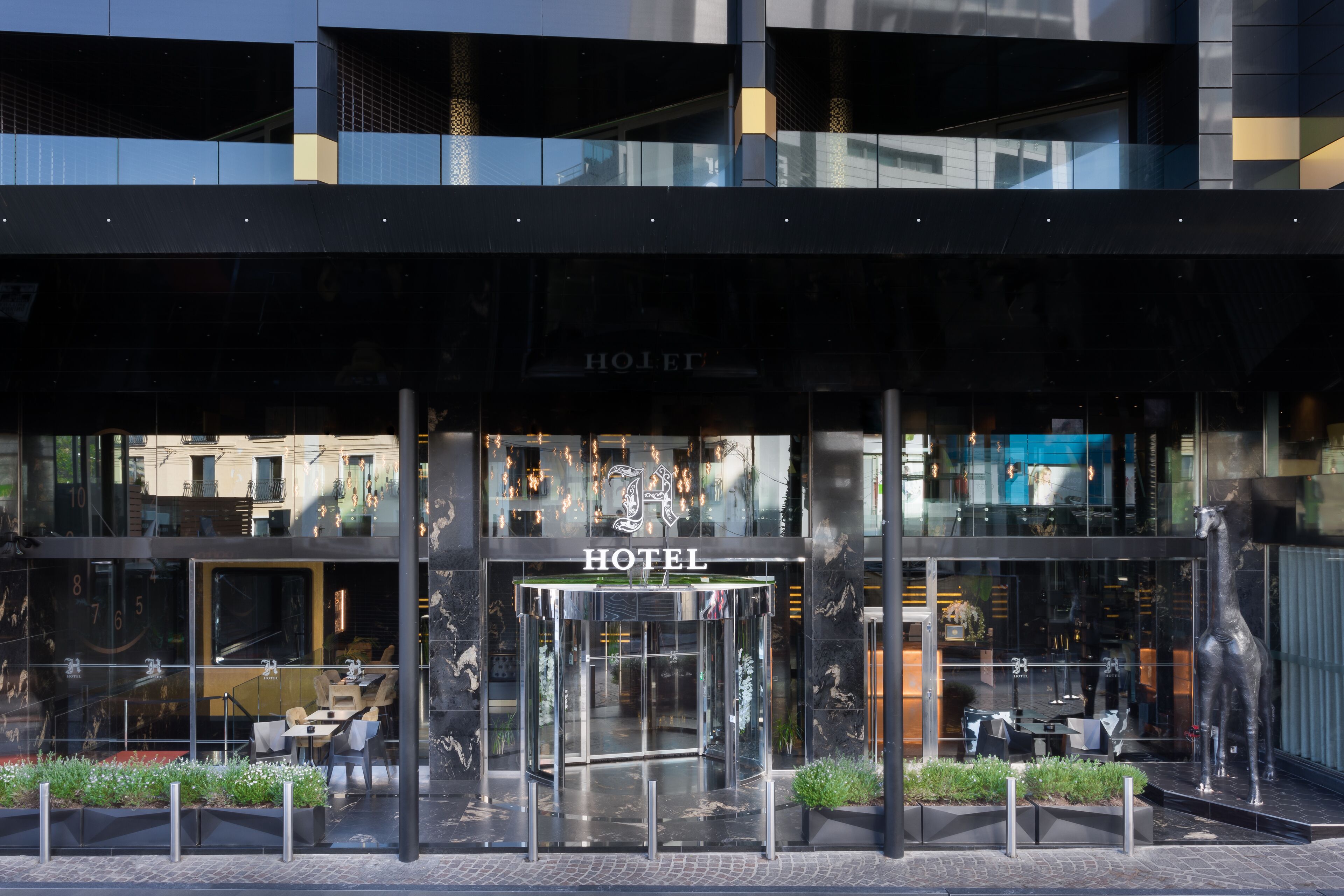 Una entrada de hotel moderna con fachada de vidrio, puerta giratoria y mobiliario exterior.
