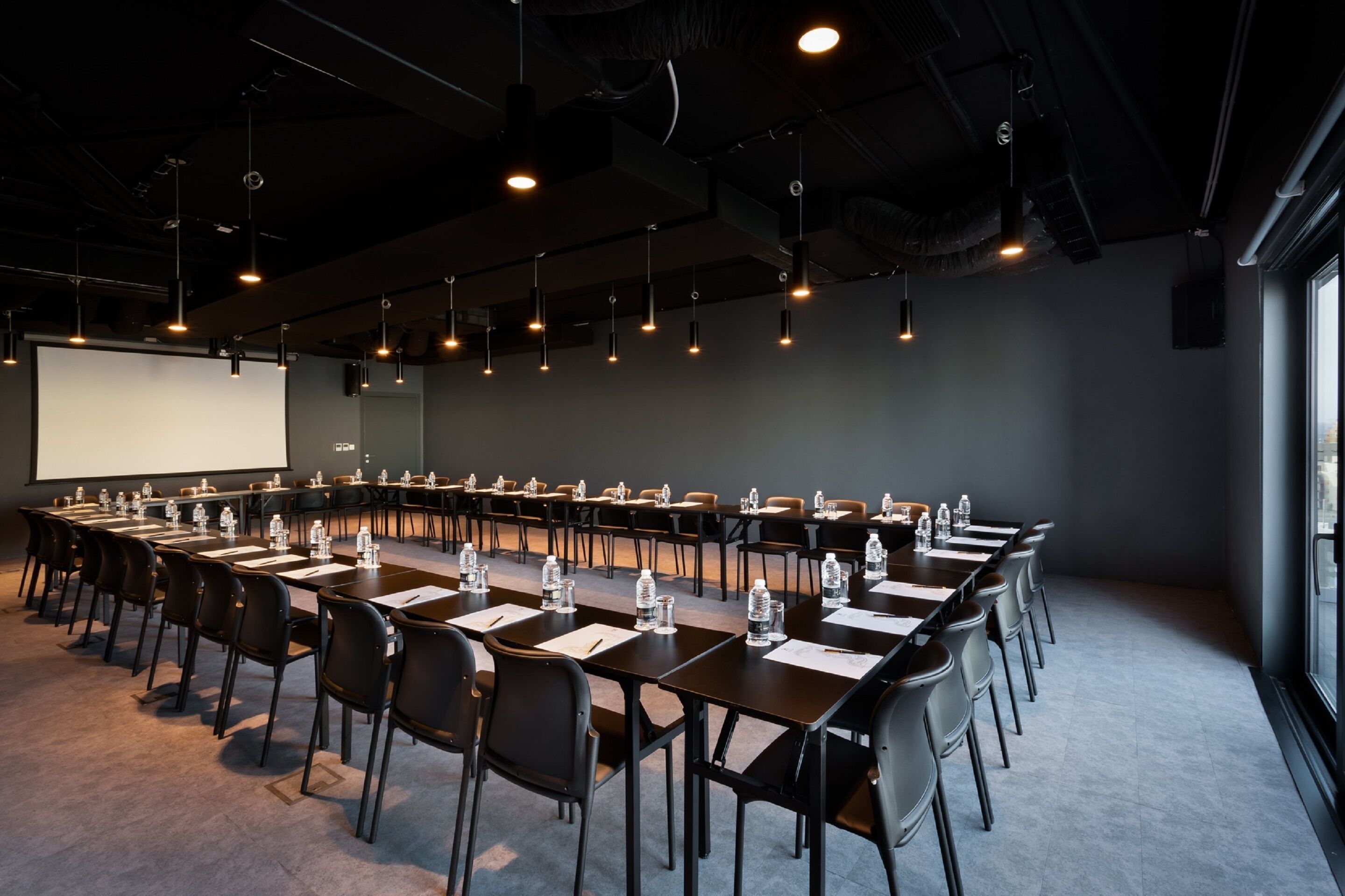 Un salón de conferencias con una larga mesa, sillas, una pantalla de proyector y un ventanal grande.