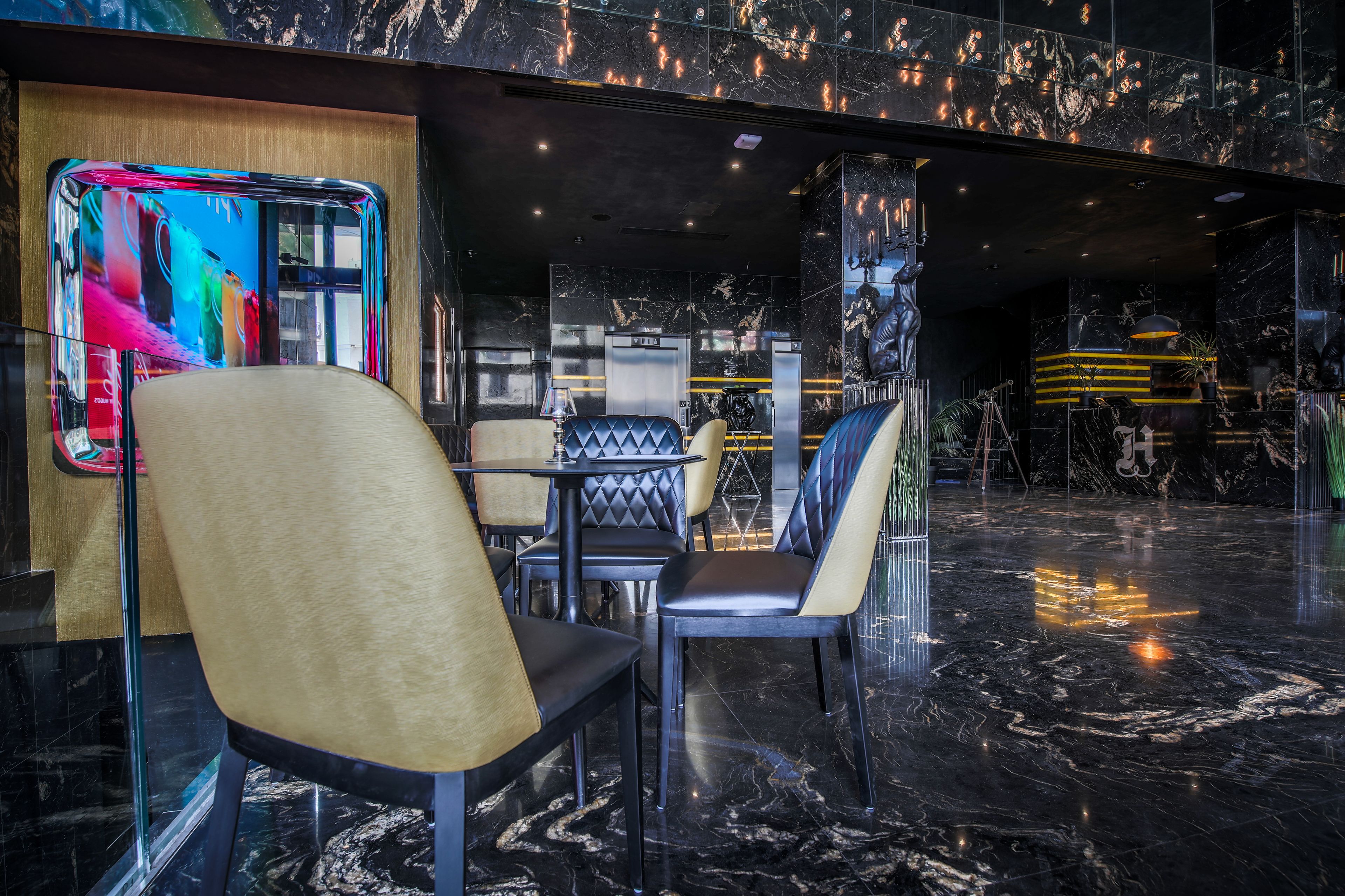 A modern interior with black marble floors, leather and metal furniture, and a large digital screen displaying colorful content.