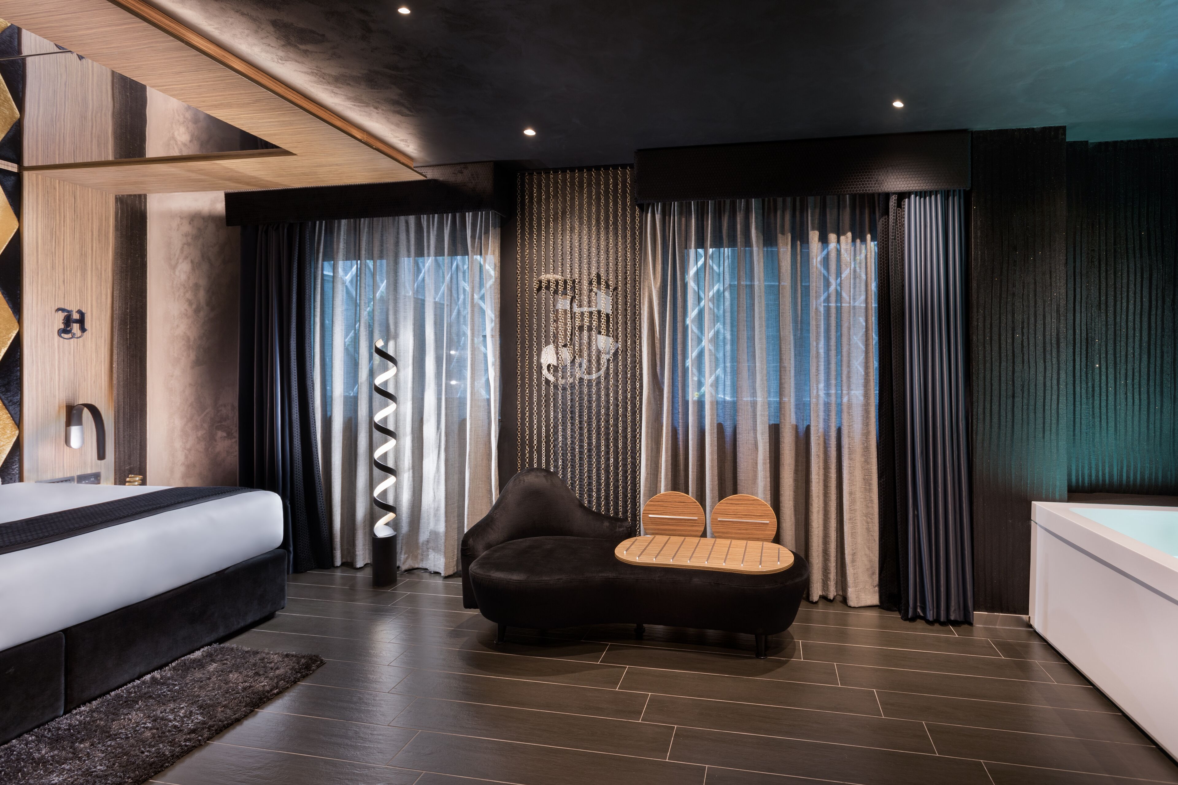 Une chambre à coucher moderne avec un lit, un canapé noir, un banc en bois et une baignoire.