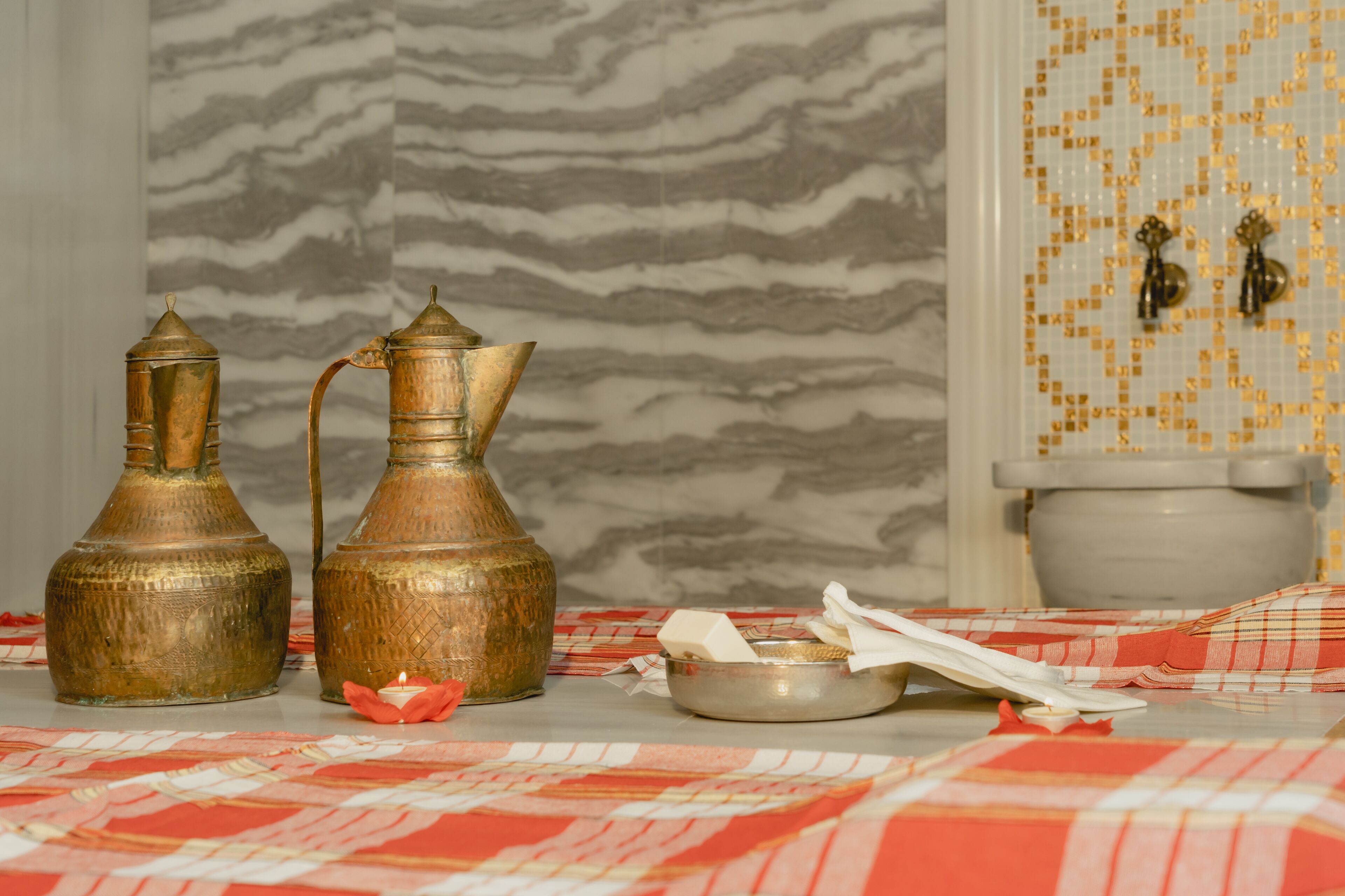 A bathroom with a marble wall, a toilet, and two brass containers on a checkered cloth.
