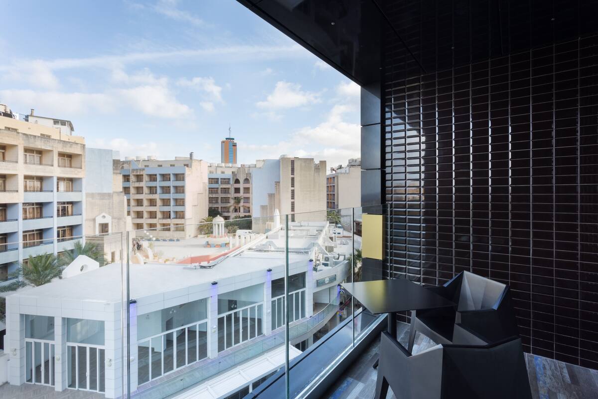 Un balcón de hotel moderno con vistas a edificios circundantes y un cielo despejado.